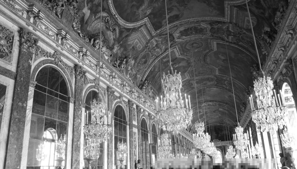 Schwarz-Weiß-Foto des Spiegelsaals von Versailles. Links Spiegel, oben mehrere Kronleuchter und ein Deckengemälde. Die Fenster rechts sind nur noch andeutungsweise zu sehen.